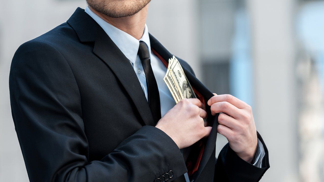 Businessman putting cash in suit pocket.