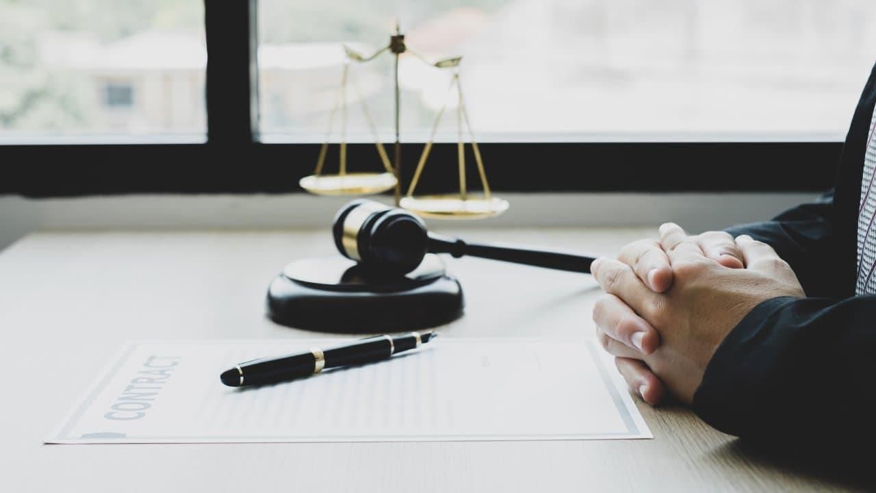 Gavel on table with man's hands crossed next to it.