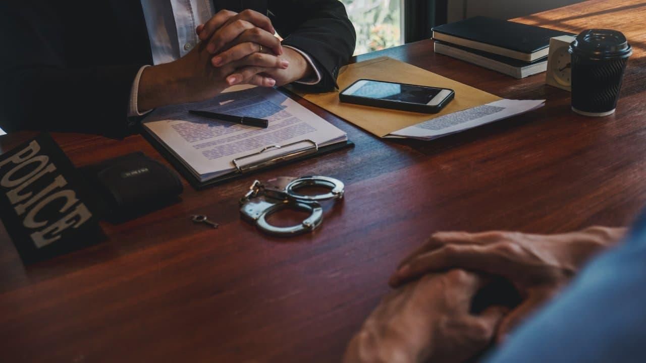 Man with hands crossed across the table with handcuffs in front of him.